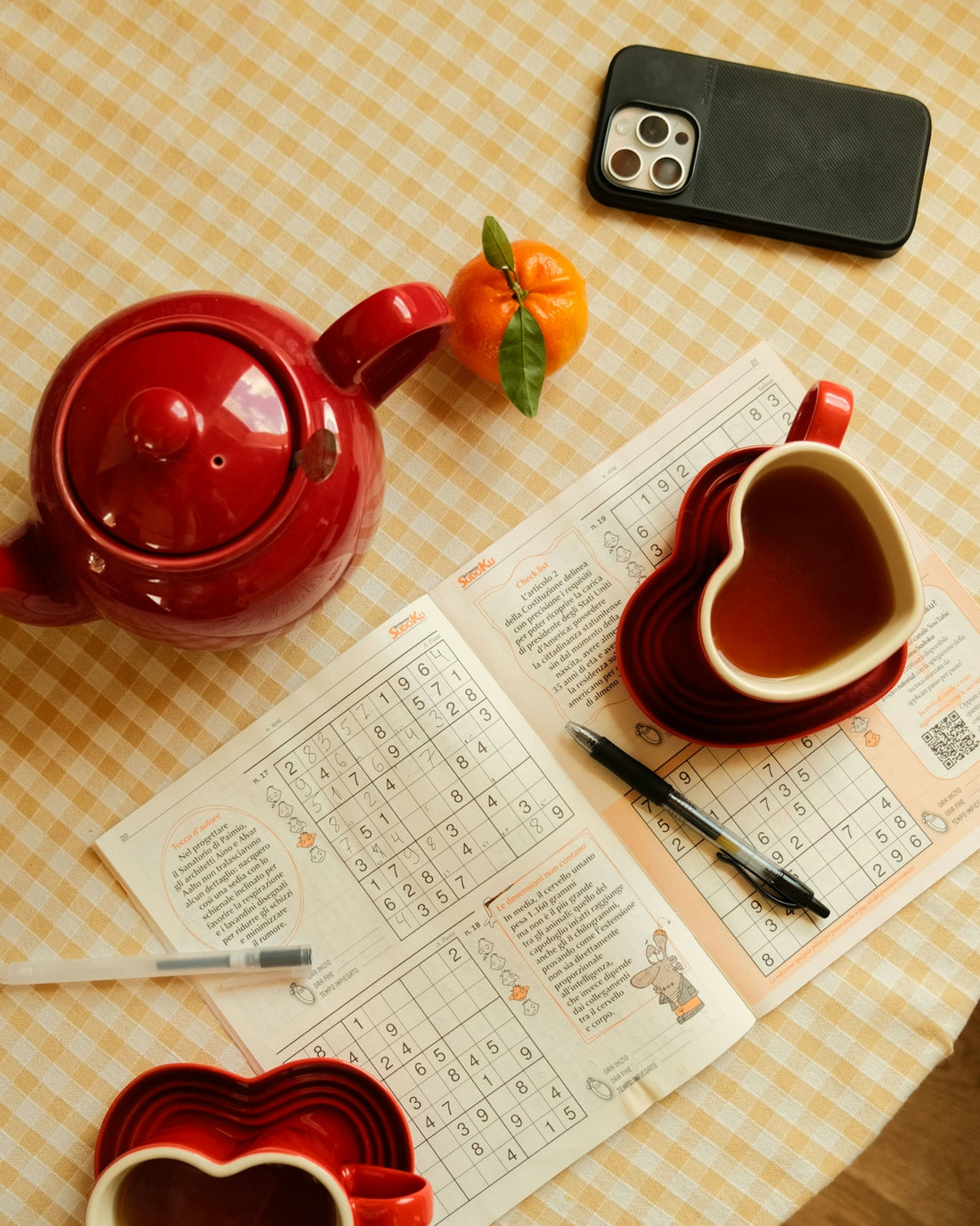 A table topped with a red tea pot next to a phone