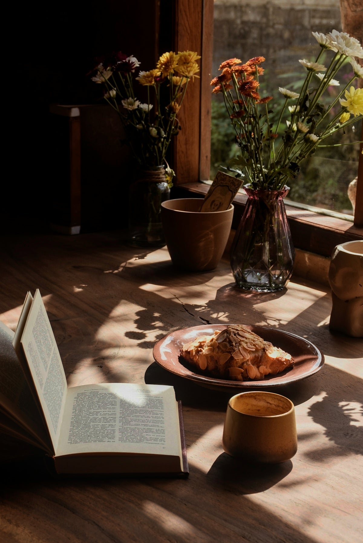 Open book, croissant, and coffee by window