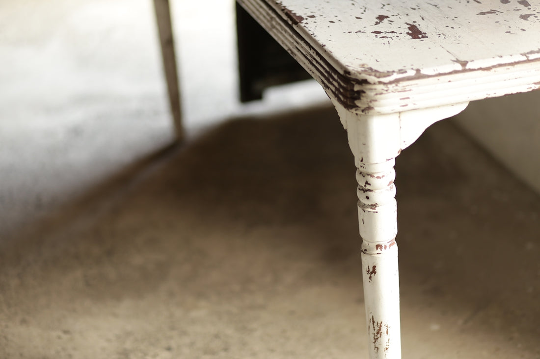 A distressed white wooden table with carved leg